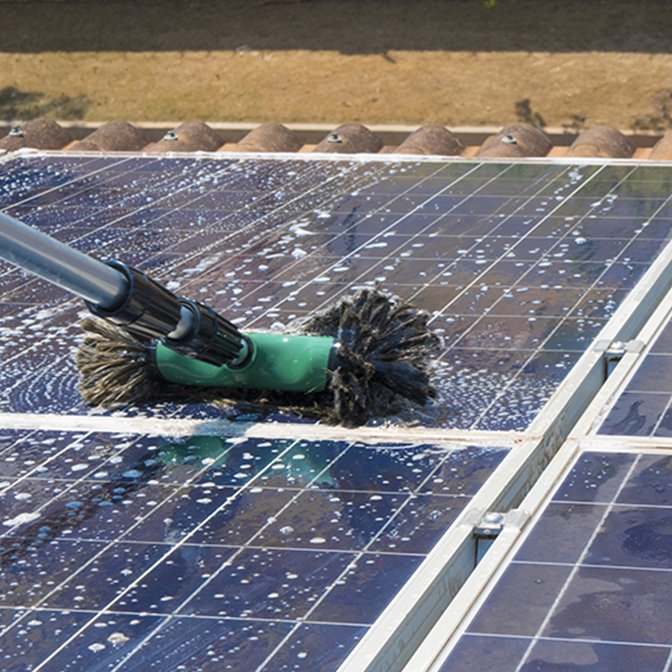 Specialist brush removing dust and grime from a rooftop solar panel array